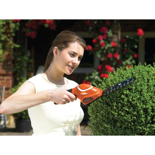 Photo of BLACK+DECKER GSL700 cordless shrub shear in use trimming a bush in a garden.