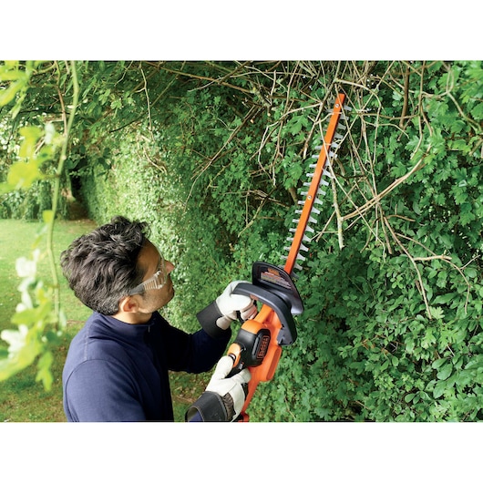 Photo of person using BLACKDECKER GTC18452PCB hedge trimmer on tall hedge outdoors.