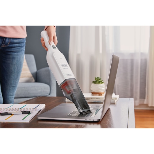 BLACKDECKER HLVC315J11 handheld vacuum cleaning laptop keyboard in home setting.