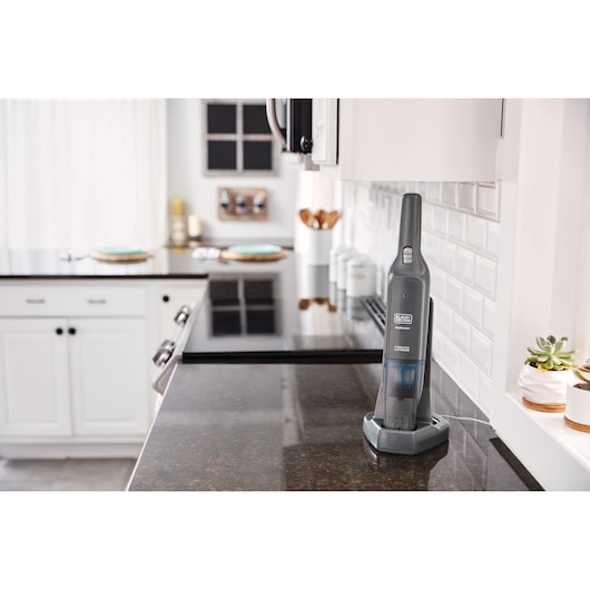 Black+Decker HLVC320B11 handheld vacuum in charging base on kitchen countertop, side angle.