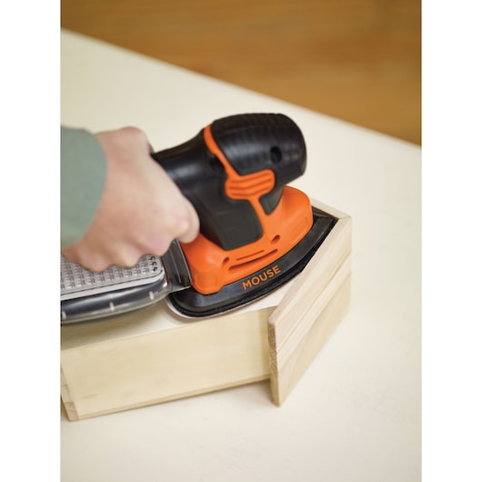 BLACKDECKER KA2500K orange and black mouse sander sanding a wooden box corner, close-up.