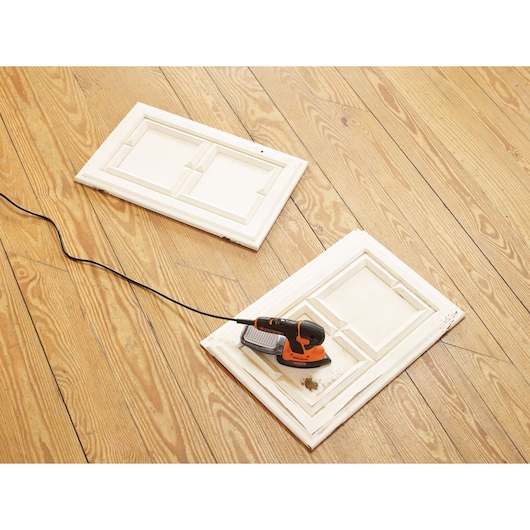 BLACKDECKER KA2500K detail sander on a white cabinet door, wooden floor background.