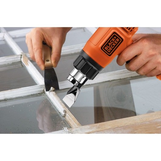 Photo of BLACK+DECKER KX1650 heat gun used to remove paint from a window frame with a scraper tool.