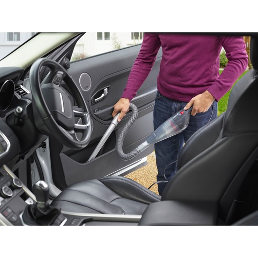 BLACKDECKER NVB12AVA handheld vacuum used to clean car interior door panel with hose attachment.