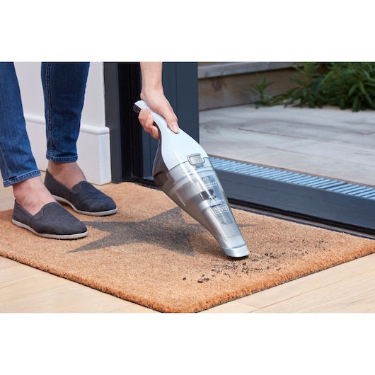 BLACKDECKER NVC215W handheld vacuum cleaning dirt from a brown doormat near a doorway.