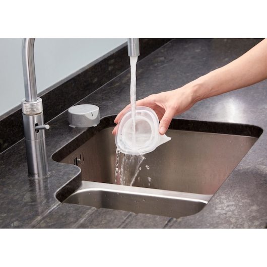 BLACKDECKER NVC215W vacuum filter being rinsed under faucet in kitchen sink, product cleaning use.