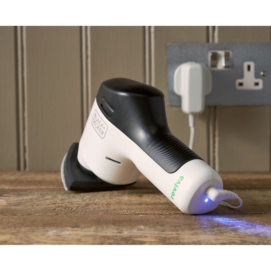 BLACK+DECKER REVDS12C handheld sander on wooden surface, white and black design, charging with blue indicator light.