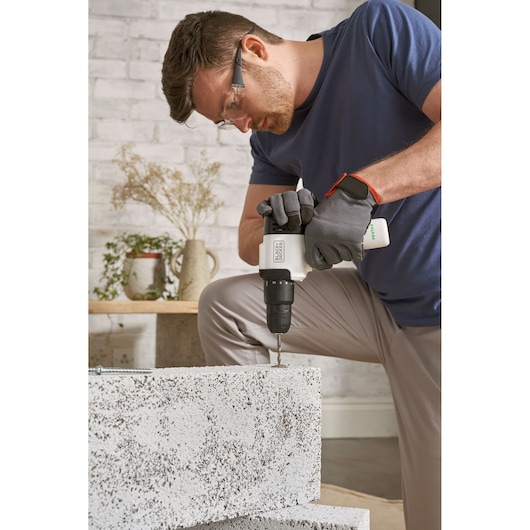 Photo of BLACKDECKER REVHD12C cordless drill in use drilling concrete block, user wearing gloves, indoor setting.