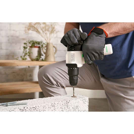 Photo of BLACKDECKER REVHD12C cordless drill in use with gloved hands drilling into concrete indoors.
