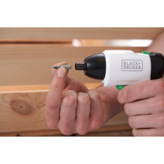 Close-up of BLACK+DECKER REVSD4C cordless screwdriver with hand holding a screwdriver bit near wood.