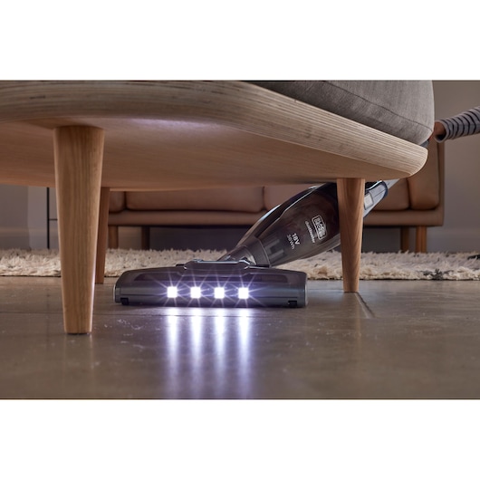 BLACK+DECKER SVB520JW cordless vacuum cleaner with LED lights cleaning under sofa, side view.