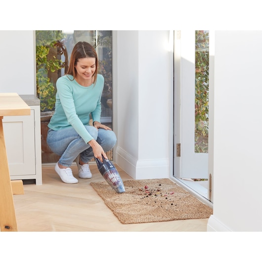 Photo of BLACKDECKER SVB520JW handheld vacuum cleaning dirt from a mat near a doorway.