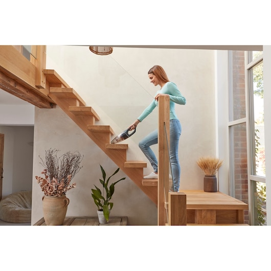 Person using BLACKDECKER handheld vacuum SVB620JW to clean wooden stairs in a bright modern home.