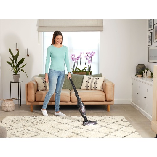 Photo of a person vacuuming a rug in a living room with a BLACK+DECKER SVB620JW cordless stick vacuum cleaner.