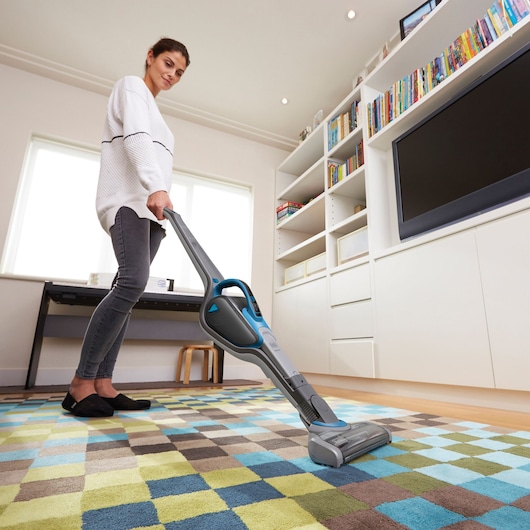 BLACKDECKER SVJ520BFS stick vacuum cleaning patterned carpet in a modern living room.