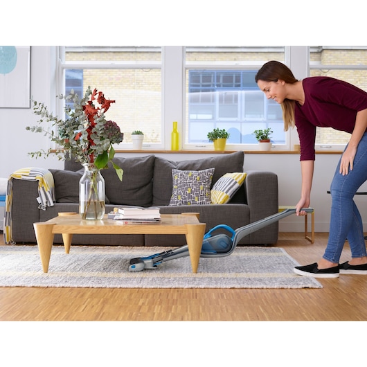 BLACKDECKER SVJ520BFS stick vacuum cleaning under coffee table in modern living room.