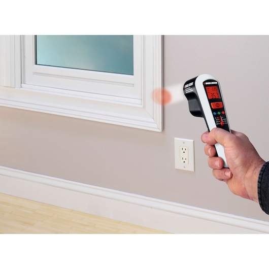 BLACK+DECKER TLD100 thermal leak detector aimed at window frame, showing temperature on display.