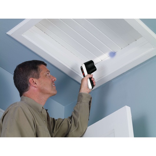 Person using BLACK+DECKER TLD100 thermal leak detector to check for drafts near a ceiling vent indoors.