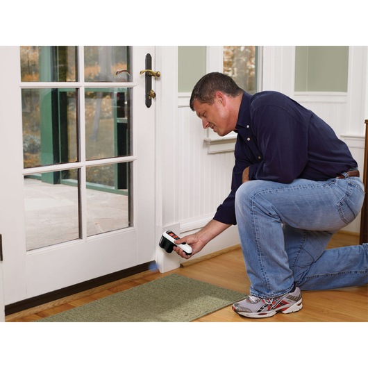 BLACK+DECKER TLD100 thermal leak detector used near white door and wall, person kneeling indoors.