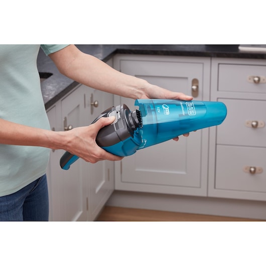A person holds and opens a blue BLACK+DECKER handheld vacuum cleaner, model WDC215WA, in a kitchen setting.