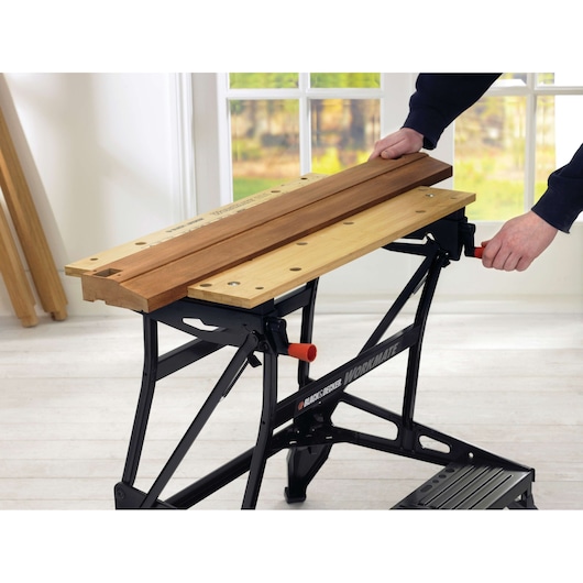 BLACK+DECKER WM626 workbench with light wood surface holding planks, indoor setting, side angle.