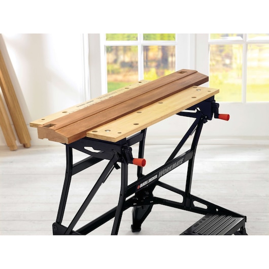BLACK+DECKER WM626 folding workbench with wooden vise and black steel frame, shown at an angle indoors.