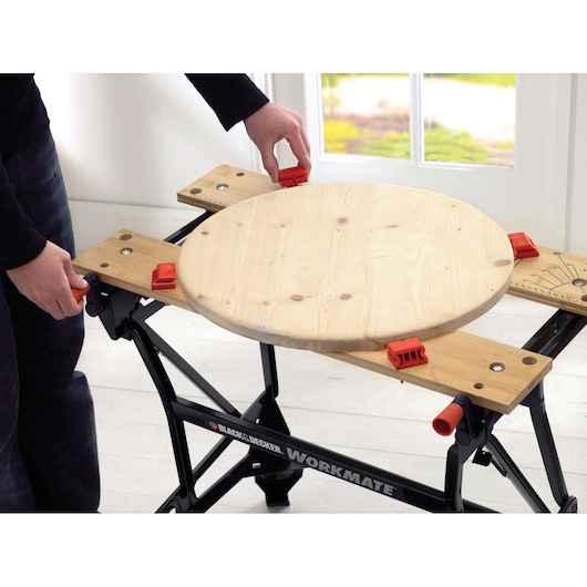BLACKDECKER WM626 folding workbench with wooden top and red clamps, front angle, holding round wood piece.